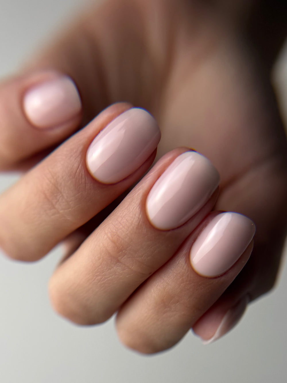 Ongles courts nude sur main gantée de noir, résultat de manucure russe
